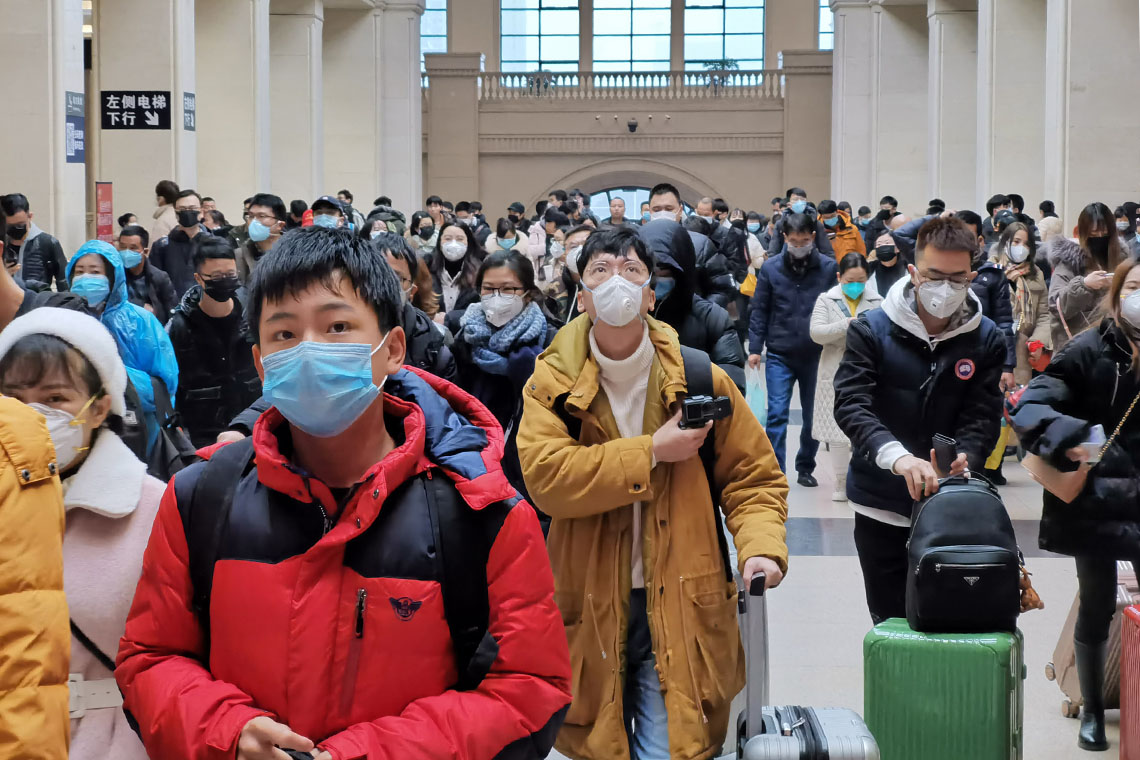 People wear face masks as they wait at Hankou railway station in Wuhan, China (photo by Xiaolu Chu via Getty Images)