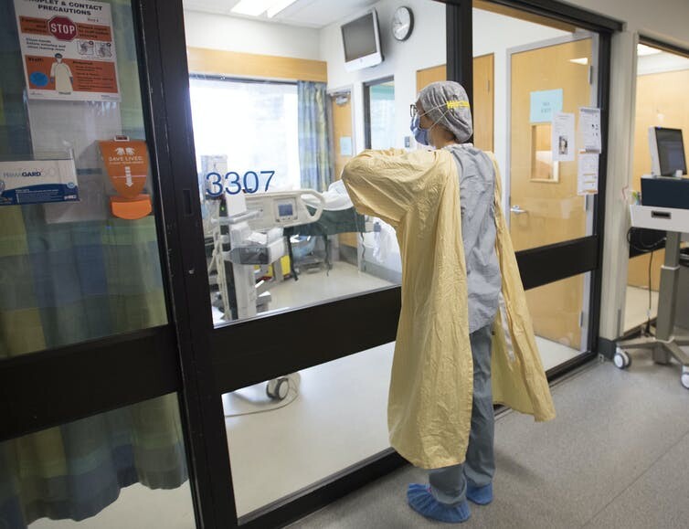  nurse puts on personal protective equipment before entering a patient’s room in a COVID-19 intensive care unit. THE CANADIAN PRESS/Jonathan Hayward